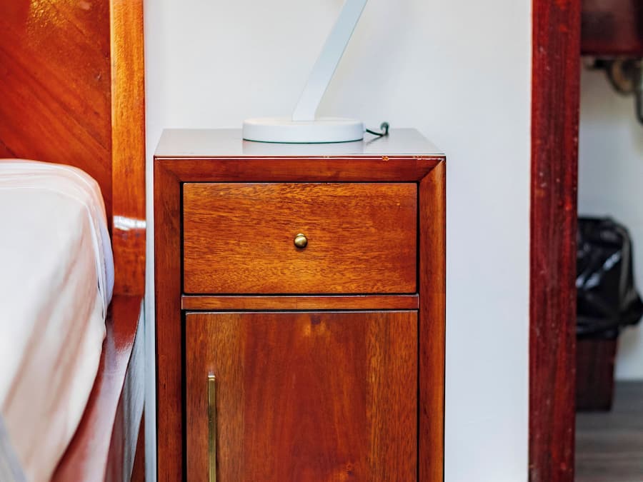 A wooden nightstand with a drawer, a lamp, and a small table with a white object on top.