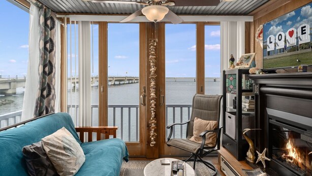 Een gezellige kamer met een blauwgroene bank, een open haard en een groot raam met uitzicht op een wateroppervlak.