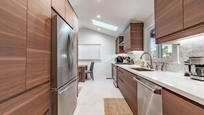 A modern kitchen with wooden cabinets, stainless steel appliances, a dining area with a table and chairs, and a skylight above. - 25% Off Sept 10-13 Mins 2 Beach, Great 4 Families! (Ventura)