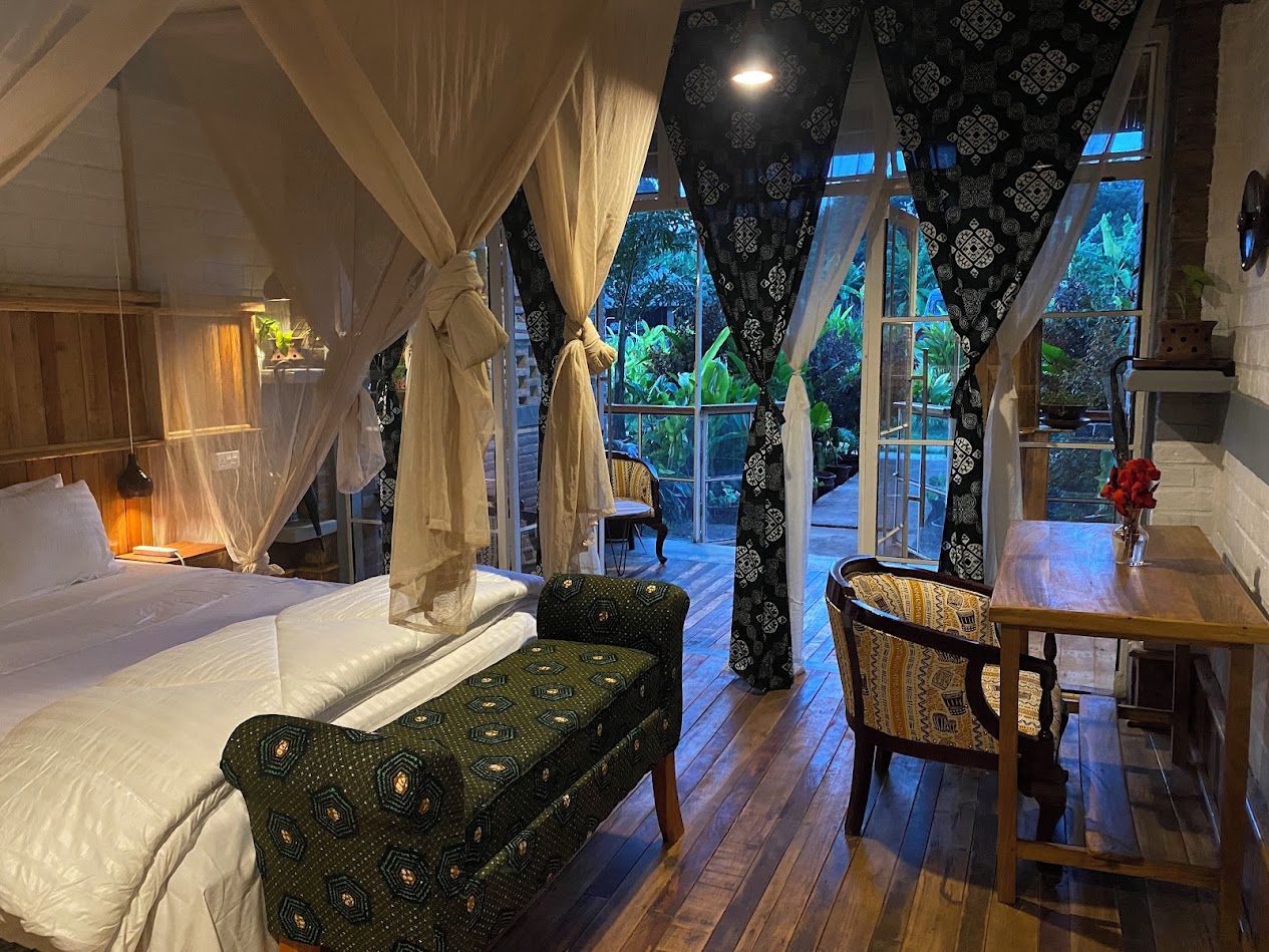 A bedroom with a canopy bed, a bench, a table, and a view of the outdoors.