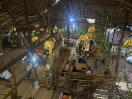 Una estructura rústica de madera con techos de paja, mobiliario de madera y lámparas esféricas colgantes.