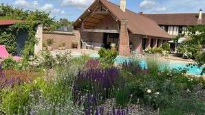 A house with a brick exterior, a large patio area, and a swimming pool surrounded by various plants and flowers. - Villa Lion-Mallet (MIANNAY)