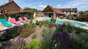 A pool area with lounge chairs, a garden with various plants, and two houses with distinct architectural styles. - Villa Lion-Mallet (MIANNAY)