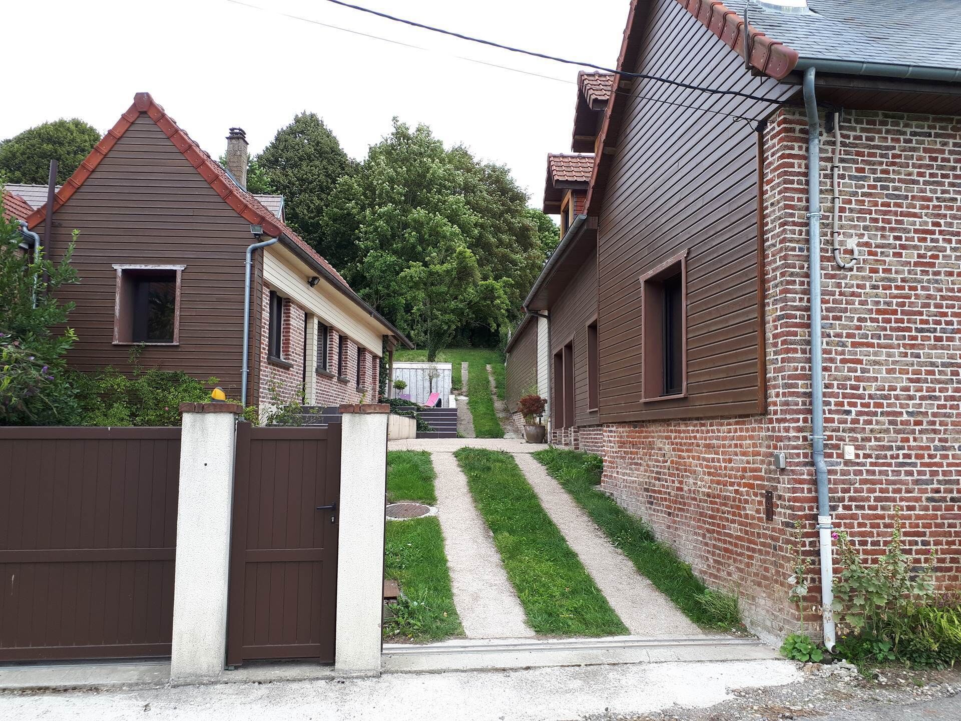 A residential area with a gated entrance, a pathway leading to a house with a sloped roof, and a brick wall.