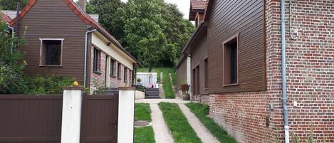 A residential area with a gated entrance, a pathway leading to a house with a sloped roof, and a brick wall.