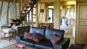 Ein großzügiger Wohnbereich mit einer schwarzen Ledersofa, einem Holztisch und einer Treppe mit freiliegenden Holzbalken.