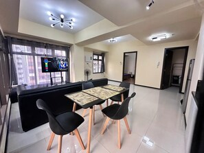 Cozinha moderna com bancada preta, área de refeições com mesa e cadeiras, e uma TV exibindo um filme.