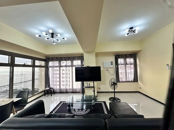 Uma sala de estar espaçosa, com janelas amplas, televisão de tela plana e ventilador de teto.