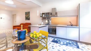 A modern kitchen with a dining area, featuring a glass table, a yellow chair, and a bottle of champagne.