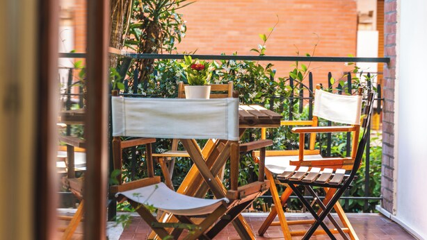 A wooden deck with a table and chairs, surrounded by potted plants and a brick wall.