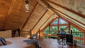 Ein geräumiges Schlafzimmer im Dachgeschoss mit Holzbalkendecke, einem Bett, einem Schreibtisch und Blick ins Freie.