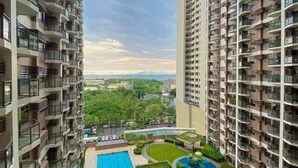 A high-rise residential building with multiple balconies, a central swimming pool, and surrounding greenery.