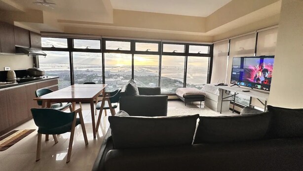 A modern living room with a large window, a dining area, and a kitchen.