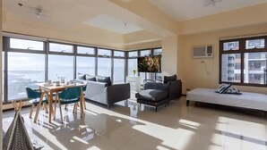 A spacious living area with a dining table, sofa, and chairs, large windows offering a view of the cityscape.