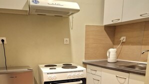 A compact kitchen with a white stove, a small refrigerator, and white cabinets. - athens.apartotel.4 (Athens)