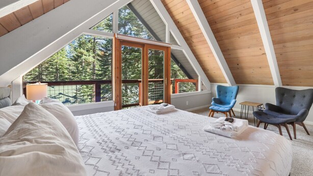 A bedroom with a large bed, a wooden ceiling, and a balcony with a view of trees. - Cozy Cabin on Brule - Hot Tub, Jungle Gym & Games (South Lake Tahoe)