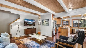 A spacious living room with a large TV, a dining area, and a kitchen. - Cozy Cabin on Brule - Hot Tub, Jungle Gym & Games (South Lake Tahoe)