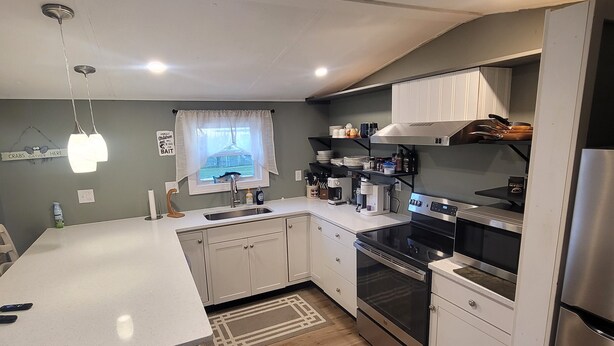 A modern kitchen with white cabinets, a stainless steel refrigerator, a built-in oven, and a window with a view of the outdoors.