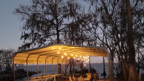 An outdoor covered seating area with tables and chairs, overlooking a body of water.