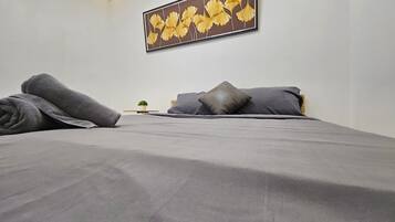 A modern bedroom with a large bed, grey bedding, a small potted plant, and a wall-mounted artwork.