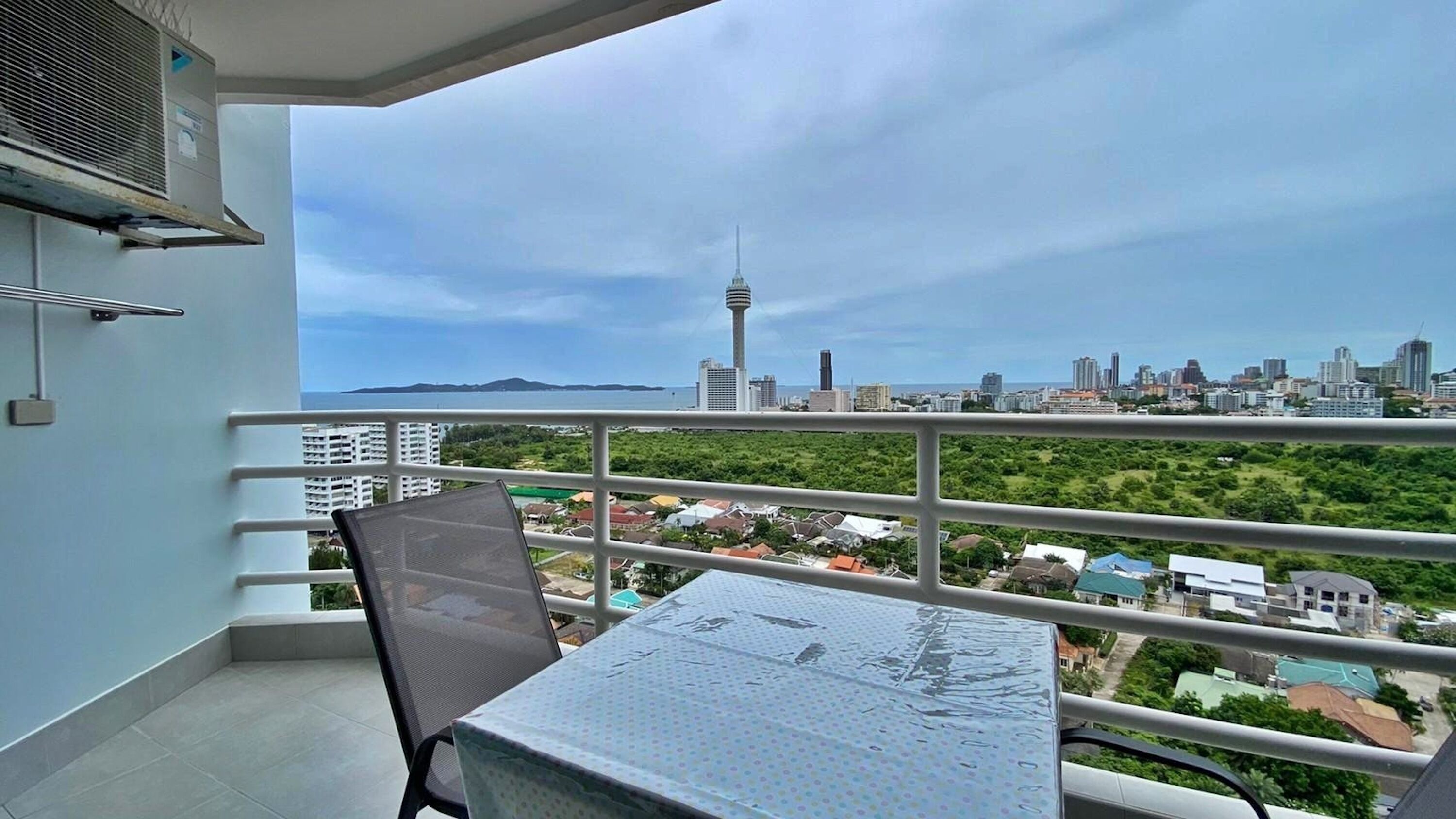 A balcony with a table and chair, overlooking a cityscape with a prominent tower and a body of water.