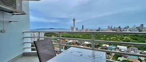 A balcony with a table and chair, overlooking a cityscape with a prominent tower and a body of water.