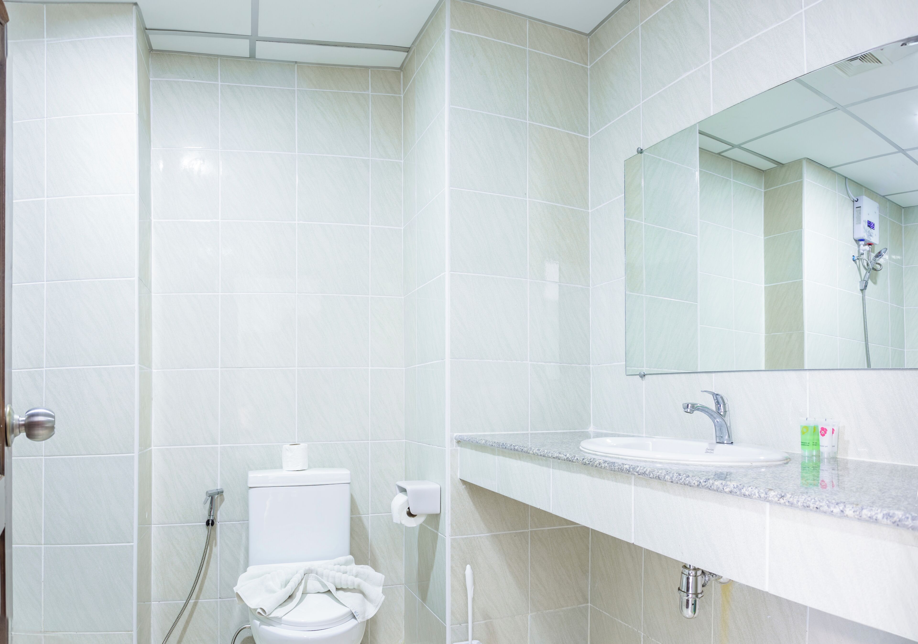 A bathroom with white tiles, a toilet, a sink, a mirror, and a shower.