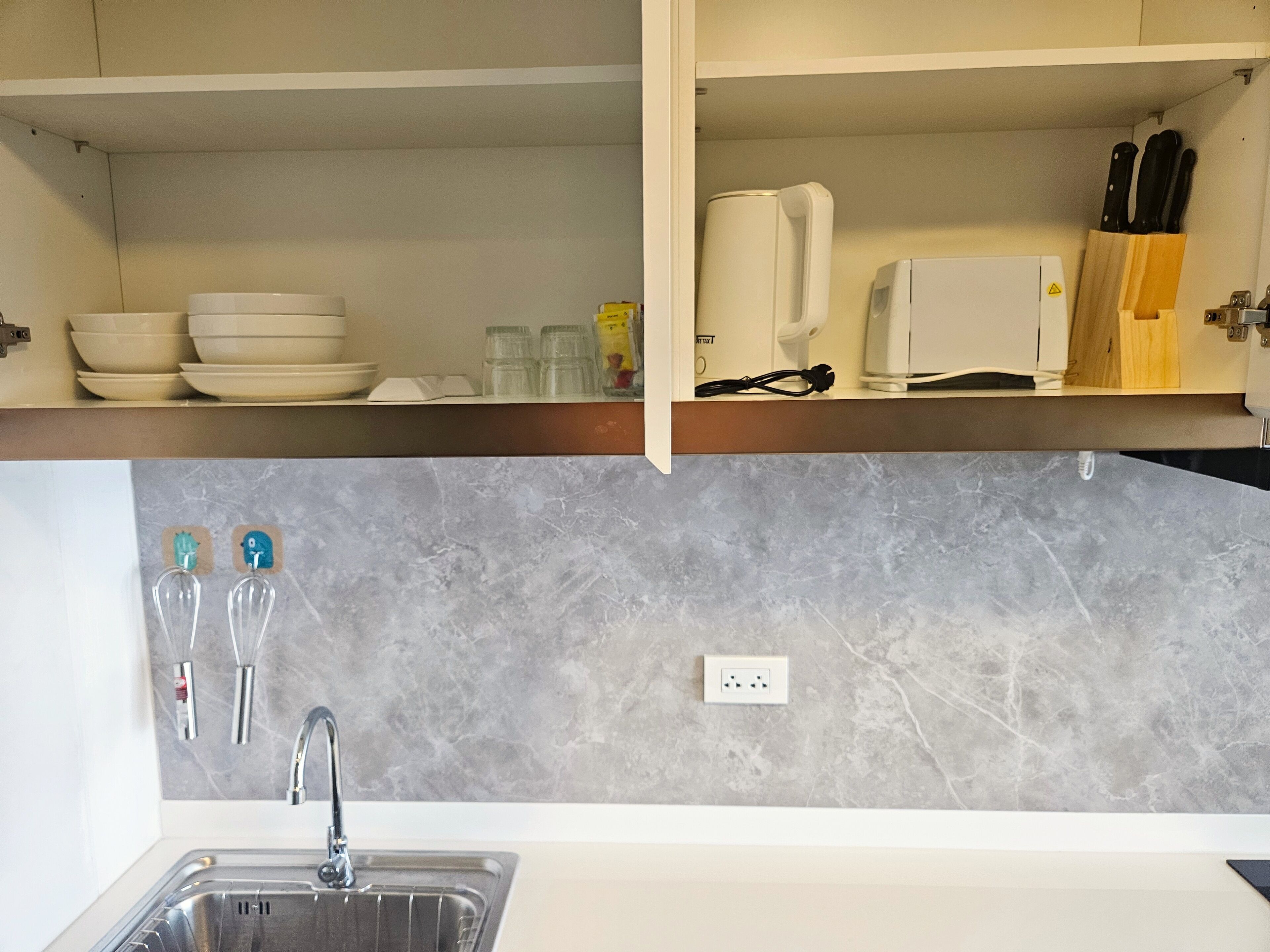 Una cocina con un lavamanos, una encimera y un salpicadero. Hay cuencos, tazas y una cafetera sobre la encimera.