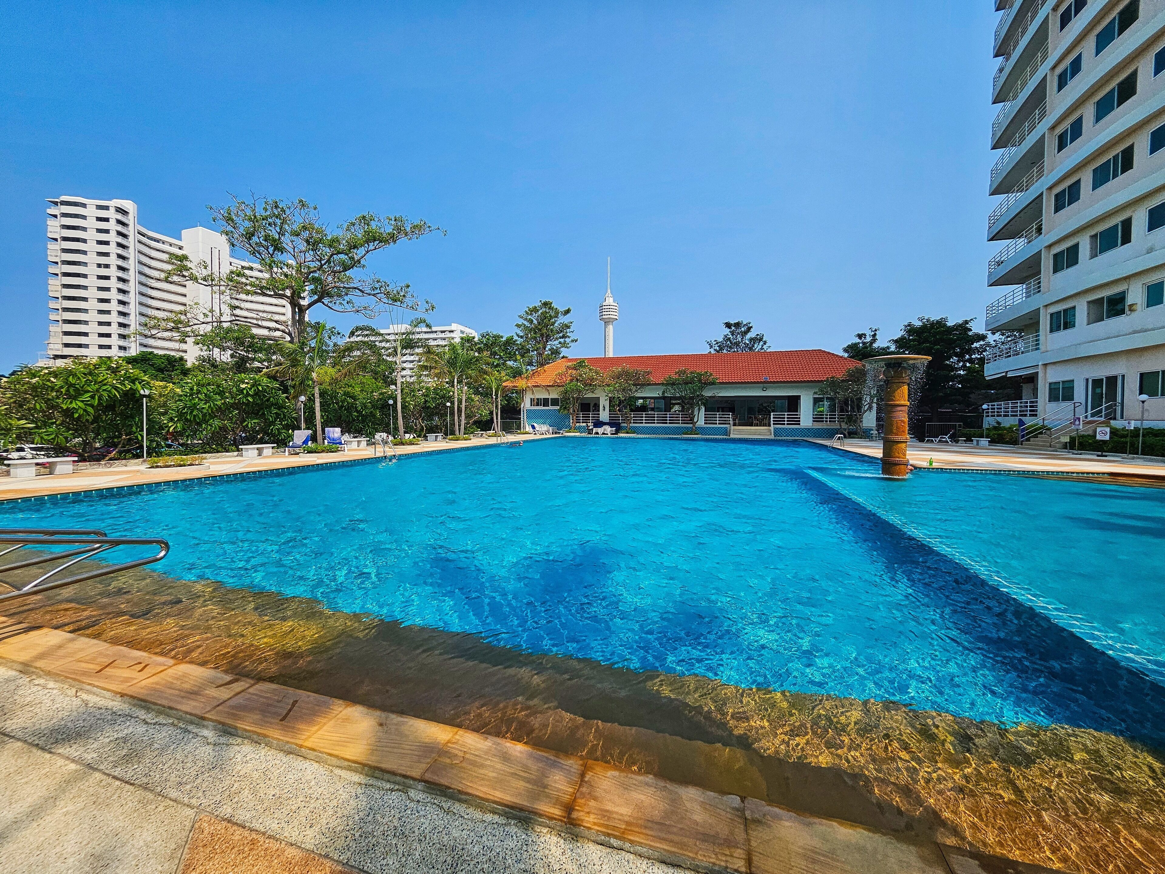 A swimming pool with clear blue water, surrounded by lounge chairs and a building with a red roof.