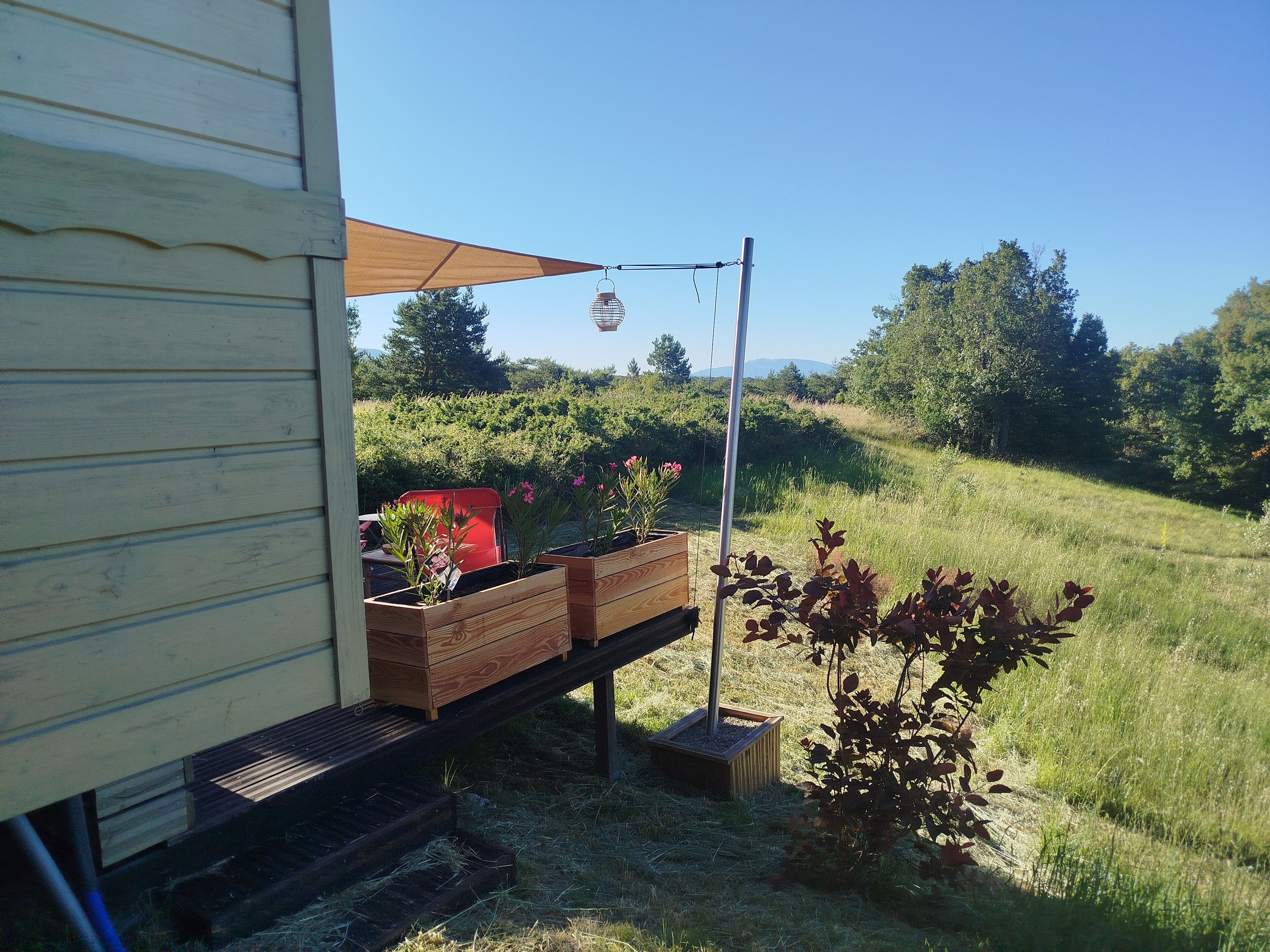 A wooden deck with a metal railing, a hanging light fixture, and a wooden planter box with plants.