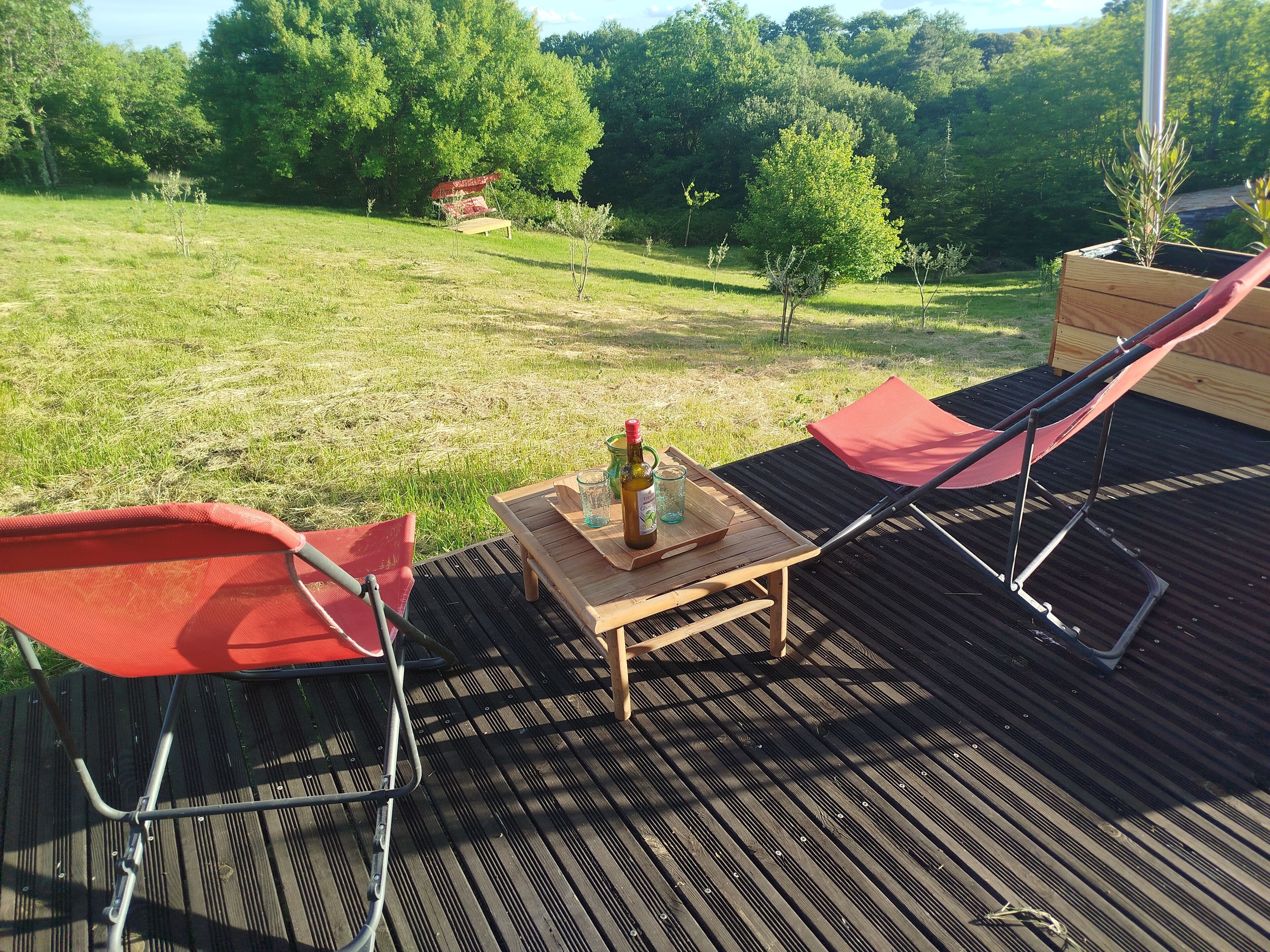 A deck with two red chairs, a wooden table, and a bottle of olive oil.