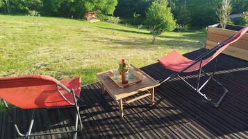 A deck with two red chairs, a wooden table, and a bottle of olive oil.