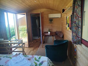 A cozy cabin interior with a wooden ceiling, a dining area with a table and chairs, a sofa, and a bed with a floral bedspread.