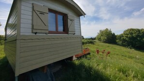 Pieni, yhden kerroksen korkuinen puinen rakennus, jossa on ikkuna ja ovi. Se sijaitsee ruohikkoisella alueella, ja taustalla näkyy puita.