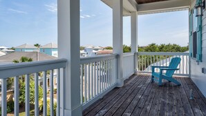 Een overdekt terras met een houten dek, een blauwe Adirondack-stoel en een witte balustrade.