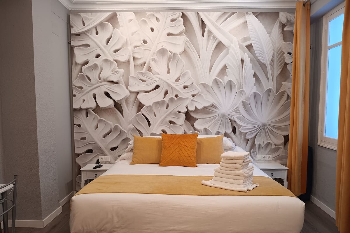 Quarto de hotel com cama grande, parede decorativa e janela com cortinas.