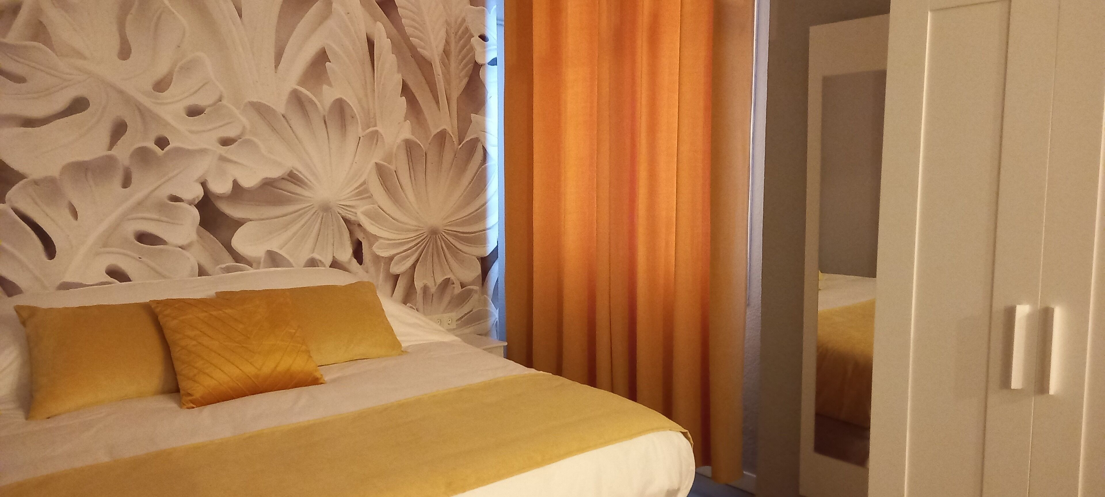 A hotel room with a bed, two pillows, a decorative headboard, and a wardrobe.