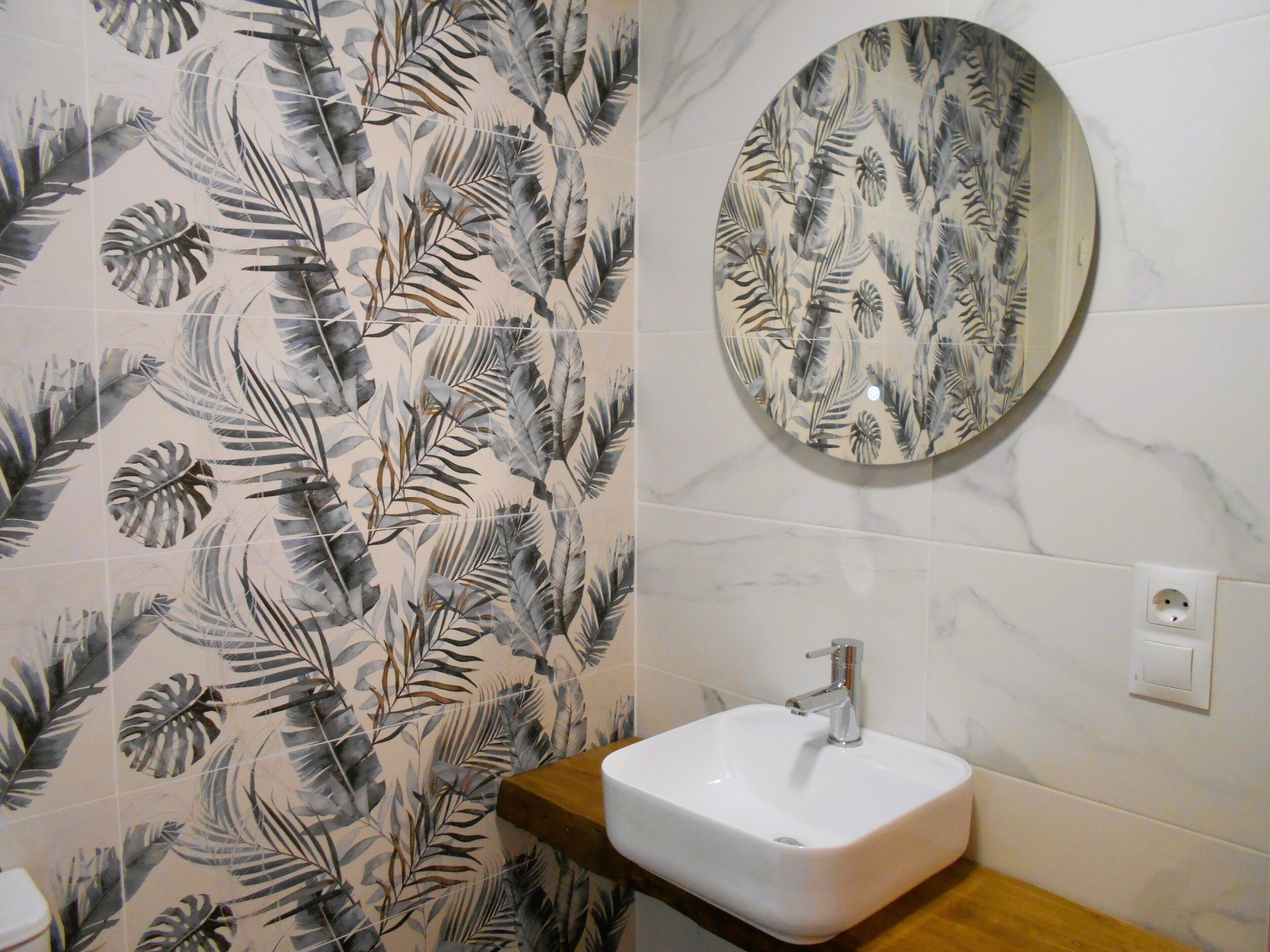 A bathroom with a white sink, a round mirror, and a shower curtain with a tropical leaf pattern.