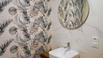 A bathroom with a white sink, a round mirror, and a shower curtain with a tropical leaf pattern.