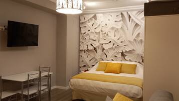 A bedroom with a bed, a TV mounted on the wall, a fire extinguisher, and a decorative wall panel.