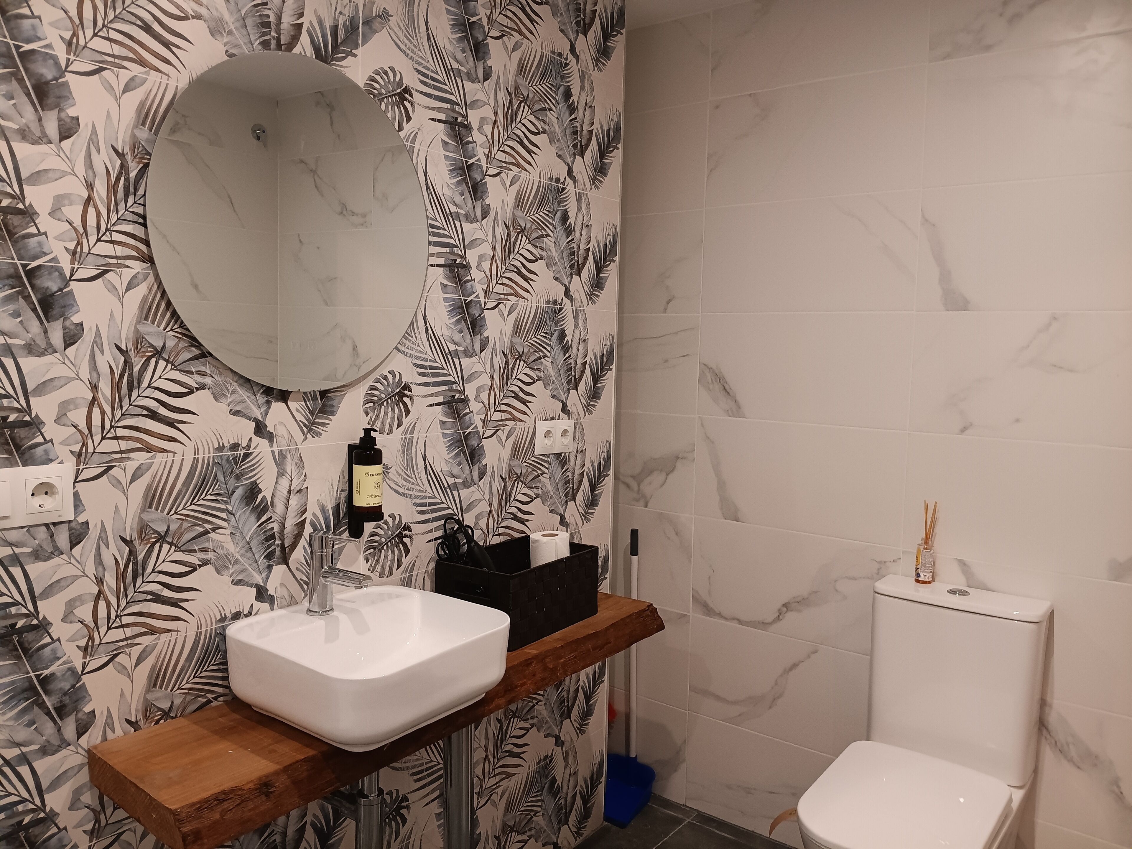 Un baño con lavamanos blanco, repisa de madera, espejo y retrete.