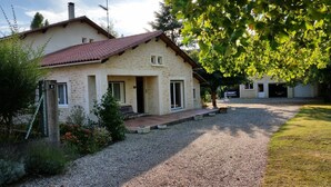Una casa in pietra con tetto in tegole rosse, un vialetto sterrato e un giardino con fiori e arbusti.