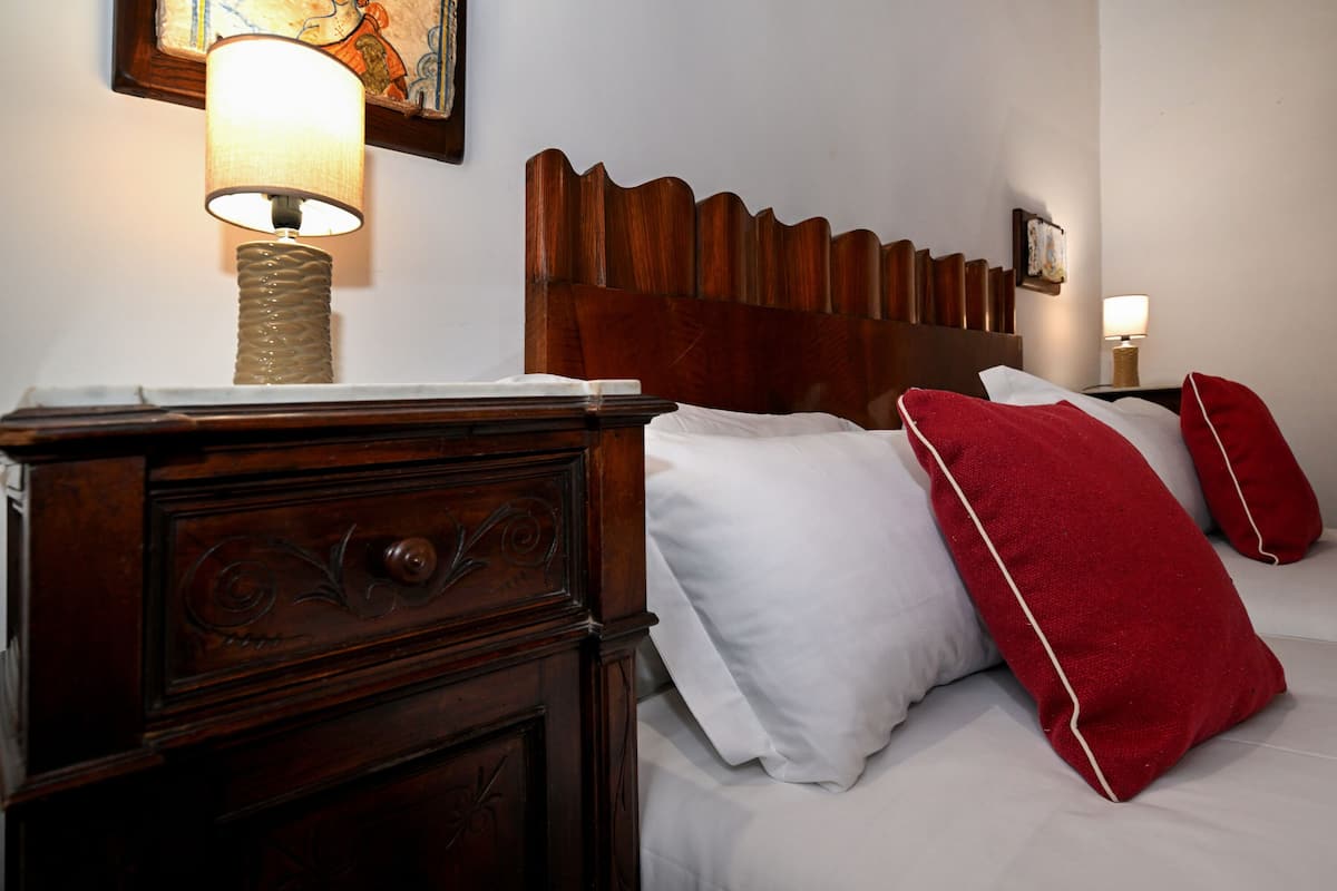 Een net opgemaakt bed met witte en rode kussens, een houten hoofdbord en een bedlampje.