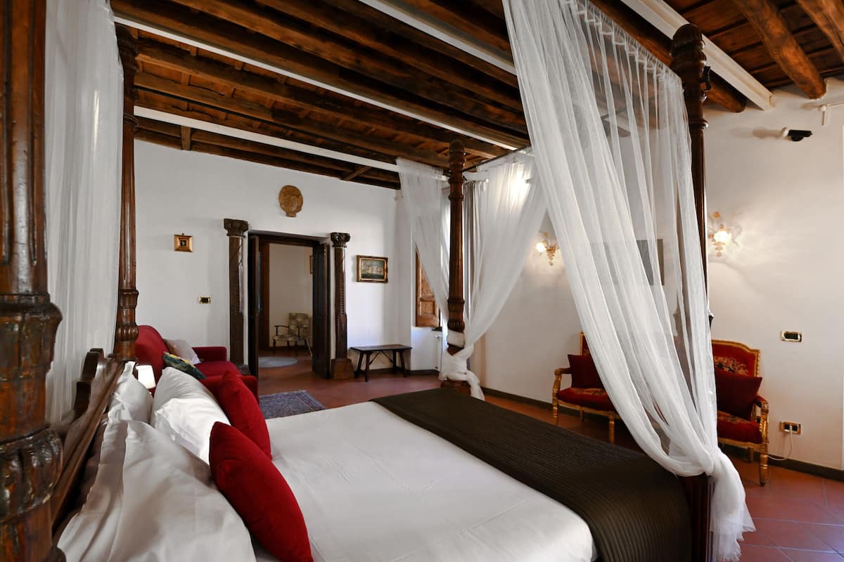 Een slaapkamer met een hemelbed, een baldakijn en een rode stoel.