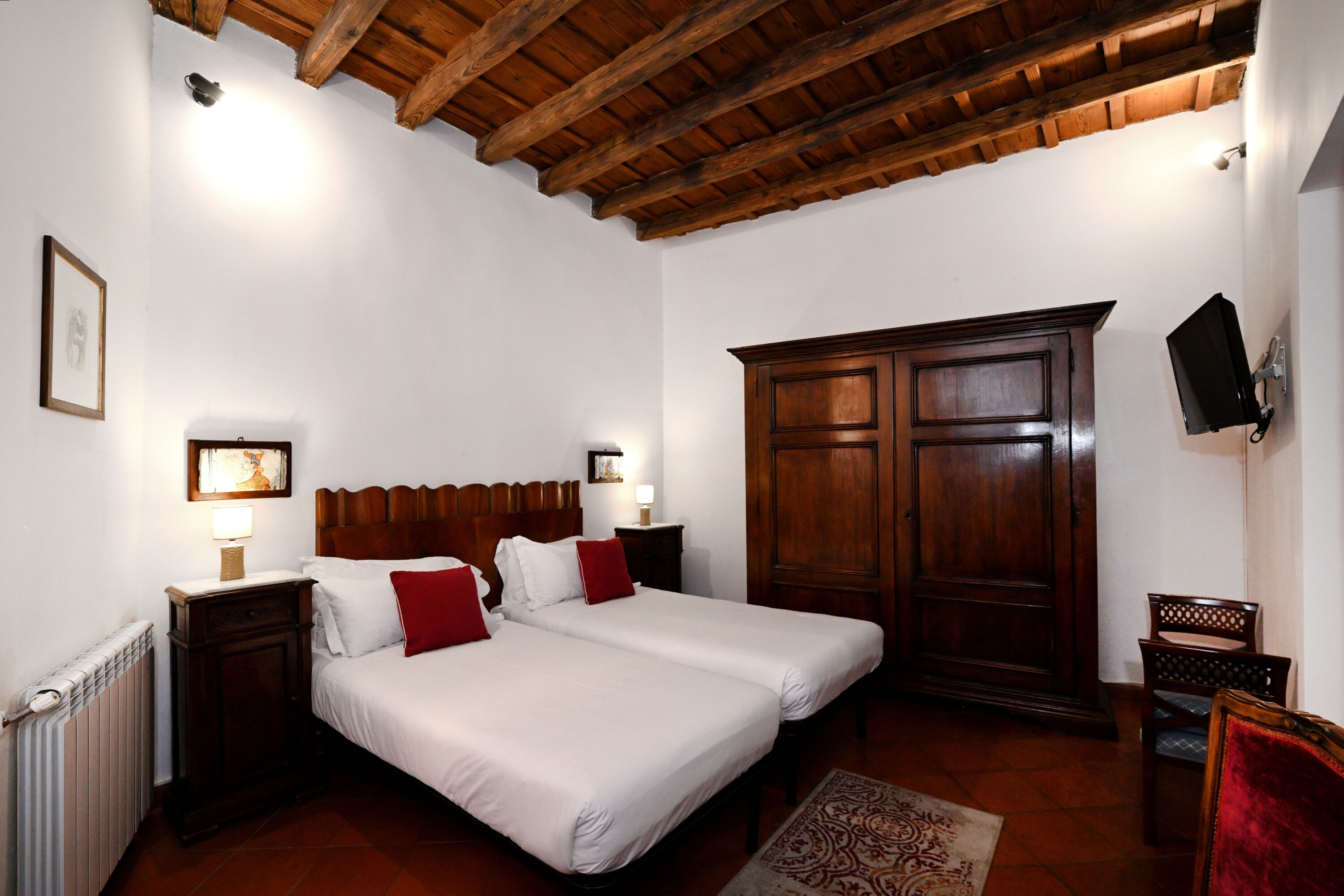 A bedroom with two beds, wooden headboards, a large wardrobe, and a television mounted on the wall.