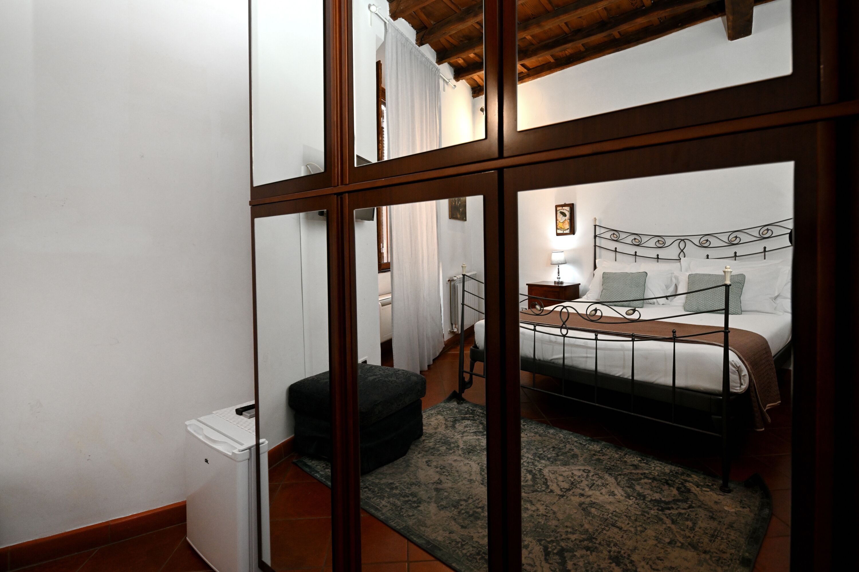 A bedroom with a bed, bedside table, and a mirror reflecting the room.
