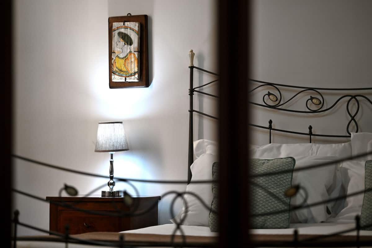Een net opgemaakt bed met witte lakens, een bedlampje en een klein houten nachtkastje.