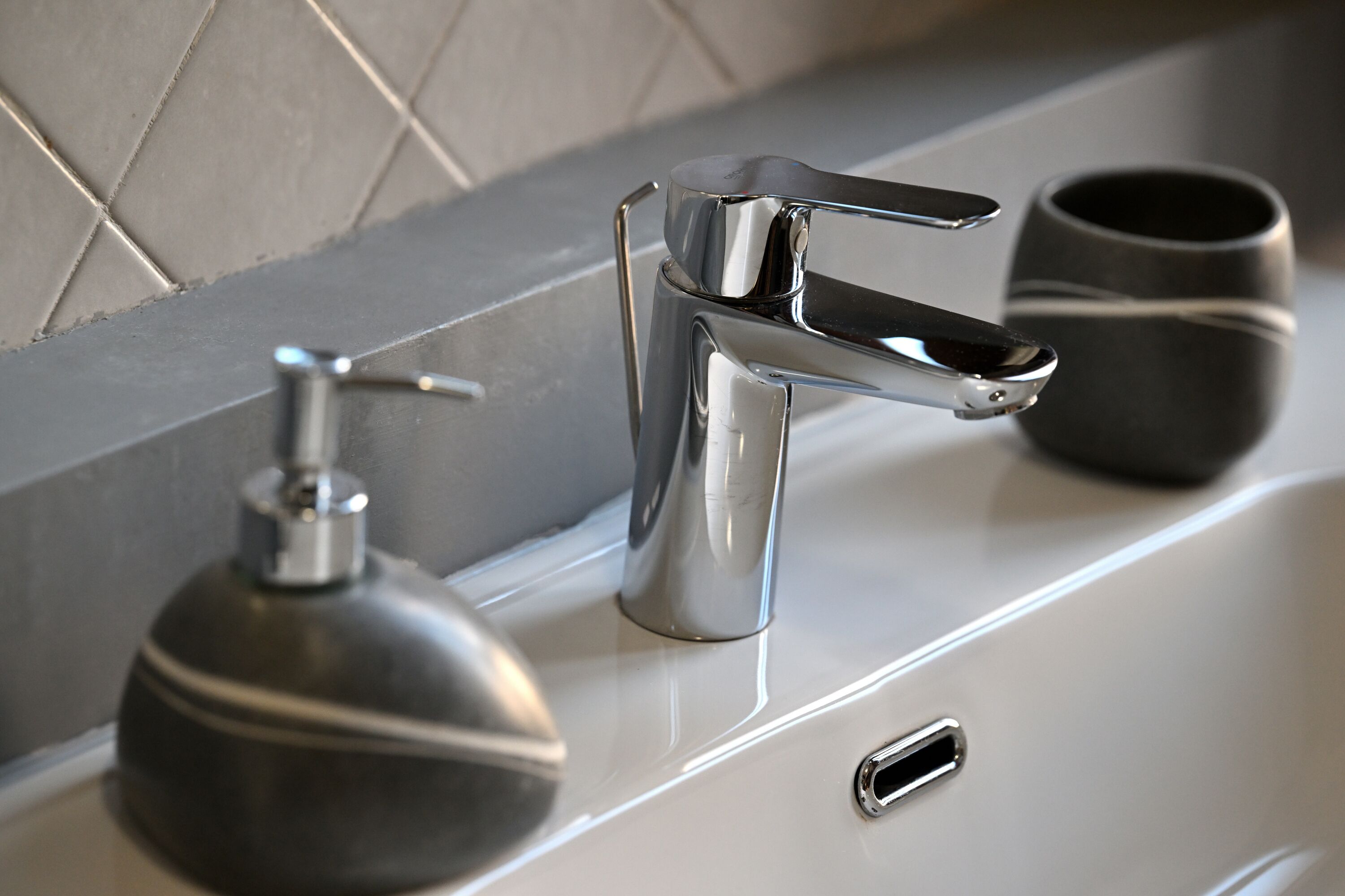 Un baño moderno con un grifo cromado, un dispensador de jabón y una taza negra en el lavabo.