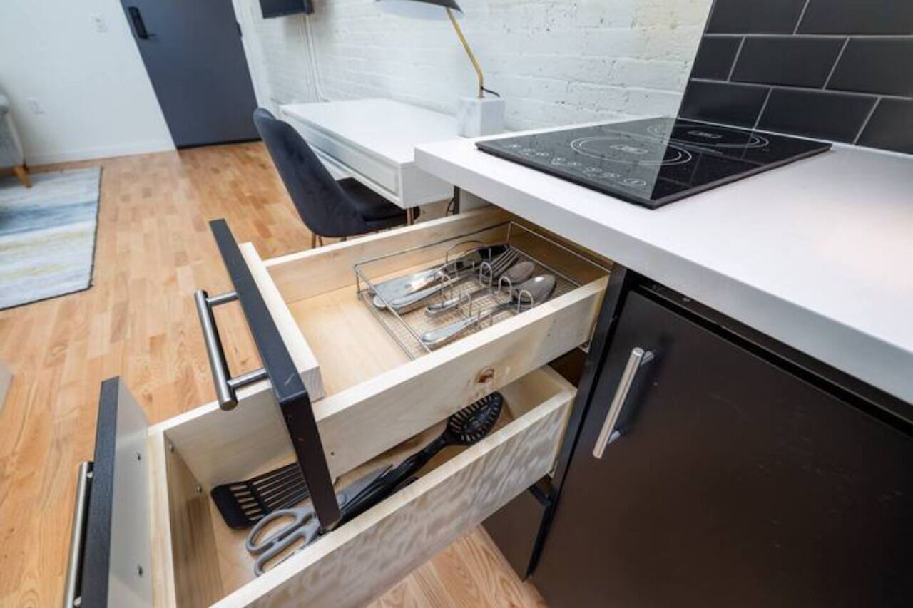 Uma cozinha com design moderno, apresentando forno embutido, bancada e gaveta com utensílios de cozinha.