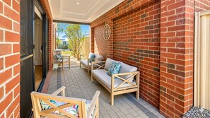 Un espace extérieur abrité, aménagé avec un mur en briques, un banc en bois et un canapé avec des coussins.